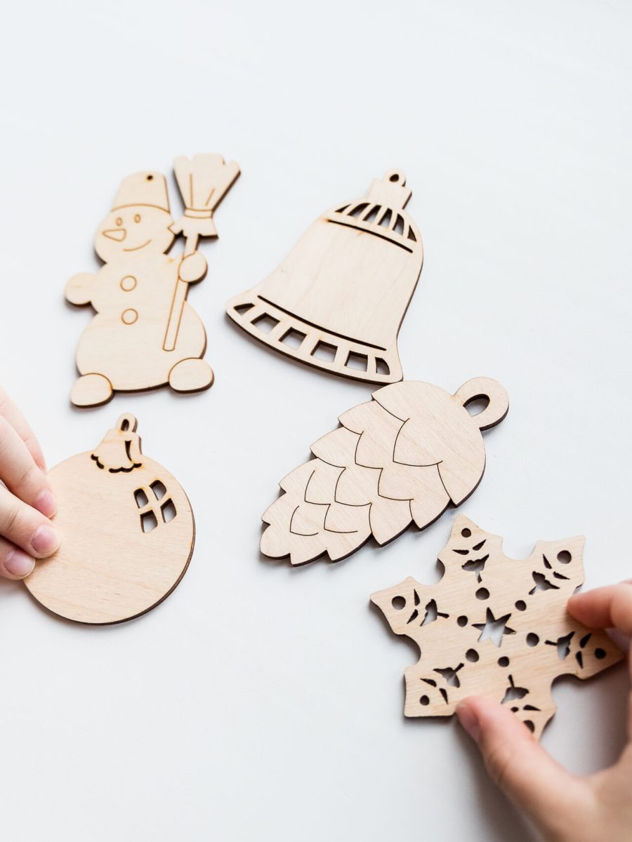 Little child painting wooden Christmas tree decorations sitting at table at home. Holiday DIY concept for children.