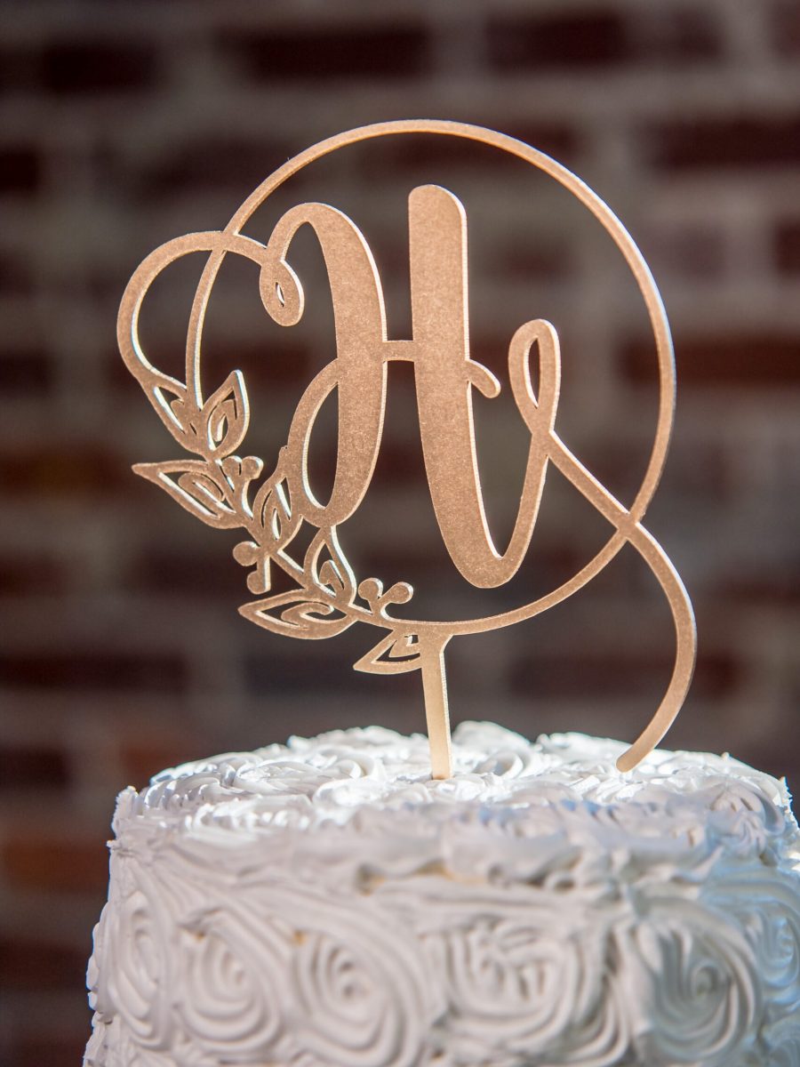 A vertical closeup shot of a H-shaped topping on a beautiful white wedding cake